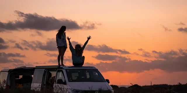 Two friends on the roof of a camper watching the sunset