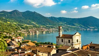 Upper Italian lakes Secret tip: View of a village at the Iseosee in northern Italy with a church tower, the sea and mountains in front of the blue sky.