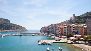 Portovenere is a secret tip in Italy: Colorful cottages in the sun next to the port of the city where some ships are standing.