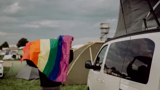 Eine Person mit Regenbogenflagge in der Hand steht neben einem Camper - der Gay Travel Index bewertet, wie LGBTQ-freundlich Länder weltweit sind.