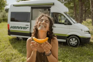 Frau lacht vor VW Grand California Campervan