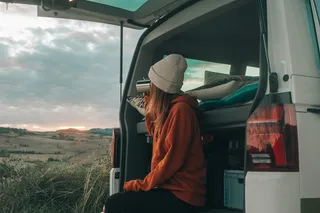 A woman sits at the edge of the open trunk of a VW camper.