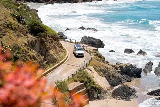 A camper runs a curvy panoramic road by the sea.