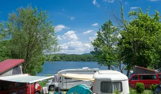 Der Campingplatz Brugger am Riegsee: Camper und Wohnmobile stehen direkt am Ufer des Riegsees zwischen Bäumen