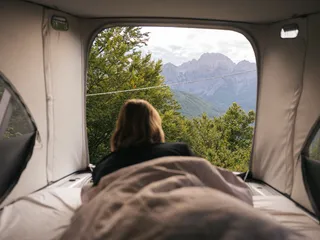 A young woman from her camper's canopy looks at a mountain landscape when camping in the Dolomites
