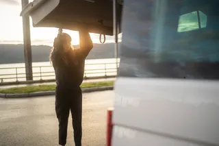 After cleaning the water tank of her camper, a young woman will close the tailgate at sunset.