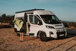 Eine Frau steht vor einem weißen Kastenwagen mit einer grünen Tischdecke in der Hand.