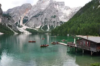 The Prague Wildsee is one of the Touri spots in the Dolomites: many tourists: in the lake are on boats, surrounded by forests and mountains.