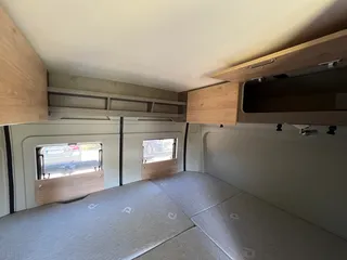 Geräumiger Camper mit großem Heckbett und praktischen Hängeschränken direkt über der Liegefläche für viel Stauraum.
