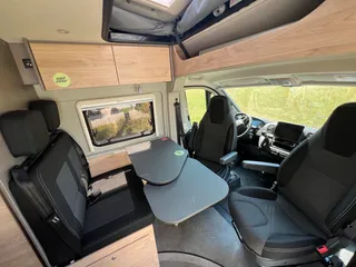 Großer Camper mit Aufstelldach mieten, gemütliche Sitzgruppe mit drehbaren Vordersitzen, ausklappbarem Tisch und Blick nach oben.