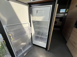 Campervan mit großem Kühlschrank mieten – geöffneter Einbaukühlschrank mit praktischen Ablagefächern in der Küchenzeile.