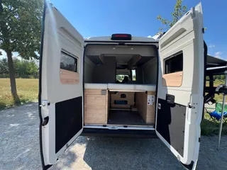 Modernen Campervan mit viel Stauraum mieten. Blick in die Heckgarage unter dem Bett mit geöffneten Türen.