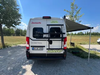 Campervan mit Fahrradträger mieten – Heckansicht des Kastenwagens mit montiertem Radträger an der Hecktür und ausgefahrener Markise.