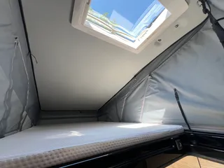 Campervan mit Bett im Aufstelldach inklusive bequemer Matratze und einem hellen Dachhimmel-Fenster.