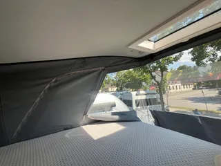 Gemütliches Bett im Aufstelldach eines Campers mit großem Ausblick durch die geöffnete Zeltwand nach draußen.
