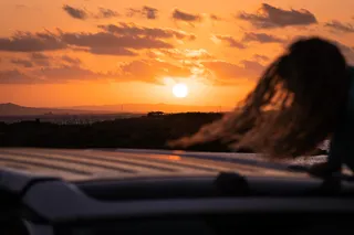 The sun goes down and a woman swings on the roof of a CamperBoys Van to watch the sunset.