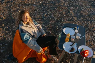 Holiday with sunshine in April: Young woman looking with closed eyes into the sun while sitting at the camping table on the beach